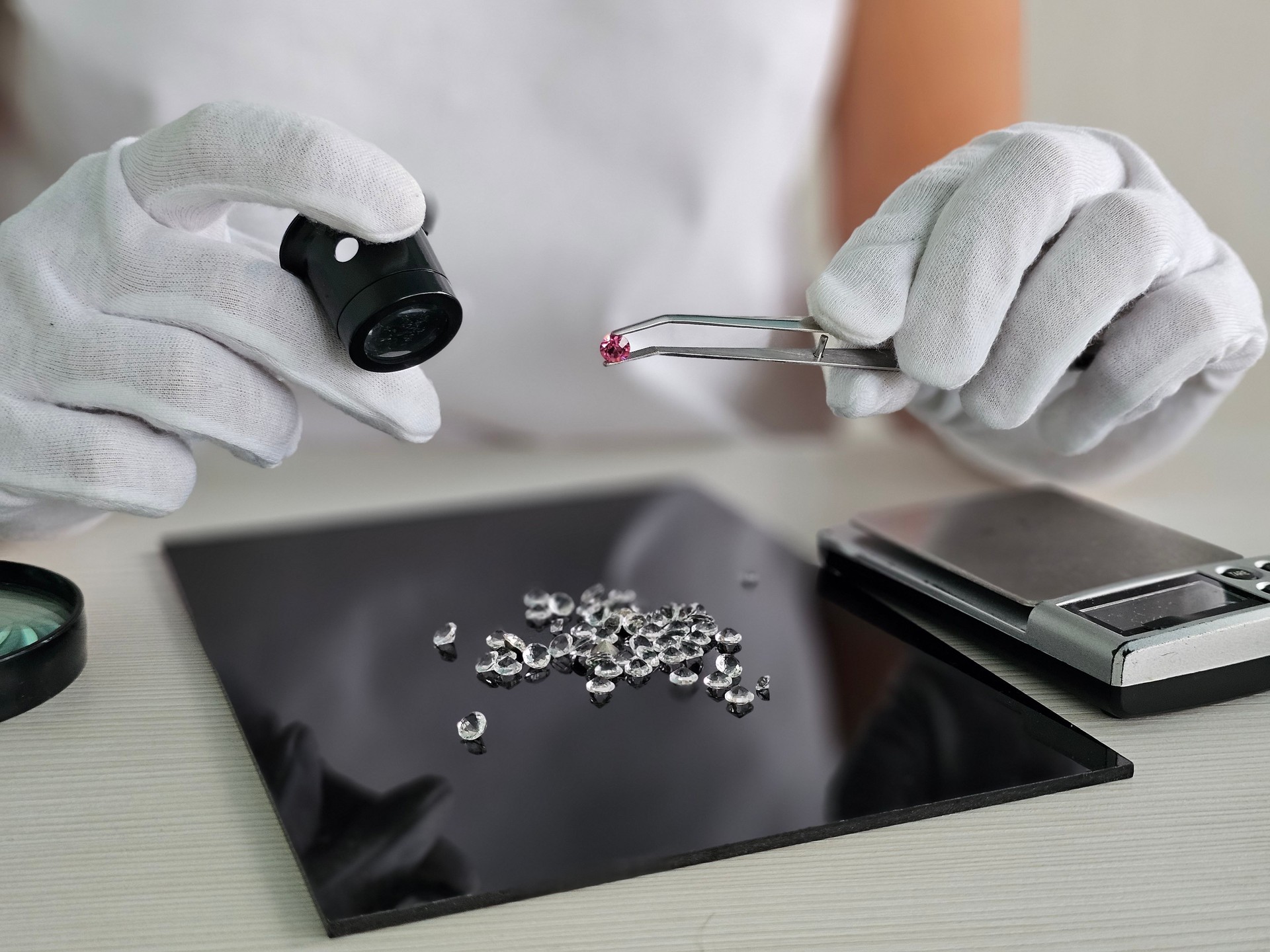 A skilled gemologist inspects sparkling gemstones using tweezers and a loupe